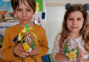 Chłopiec i dziewczynka pokazują udekorowane akrylowe jajka.